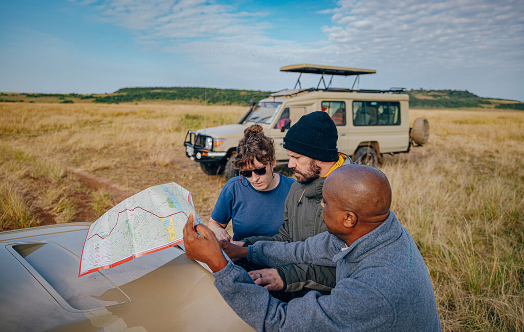 Two tourists and a safari guide looking at a map to see how to travel to Kenya; a safari vehicle in the background.