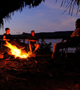 Three people sitting around a campfire at night.