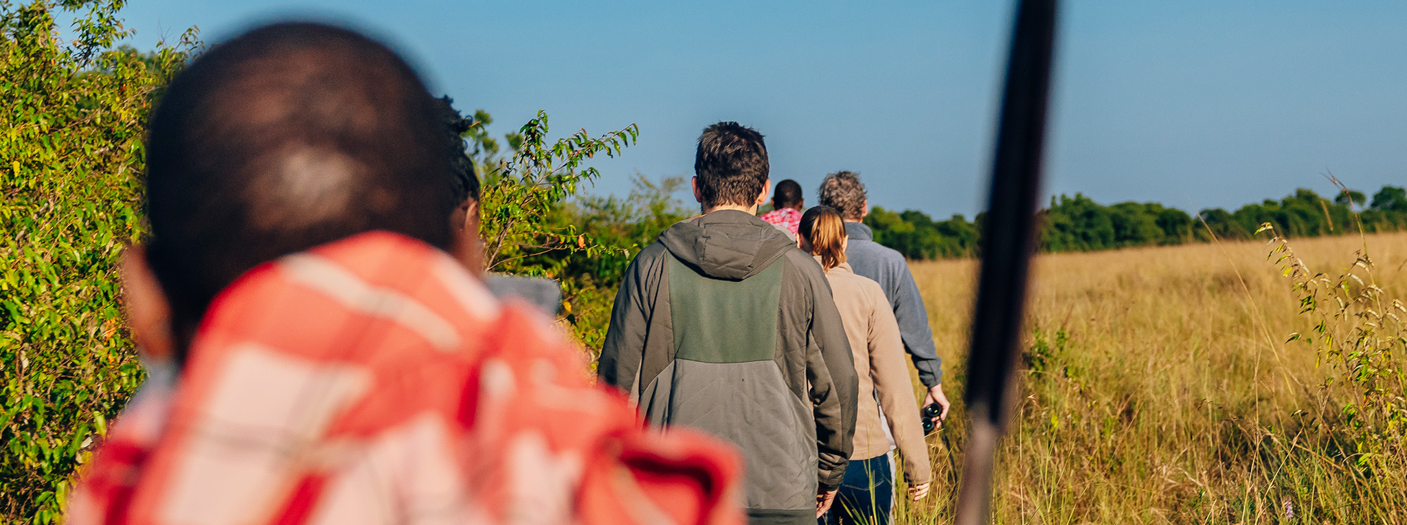 A group of people on a bush walk with a Maasai guide during a Kenya family safari.