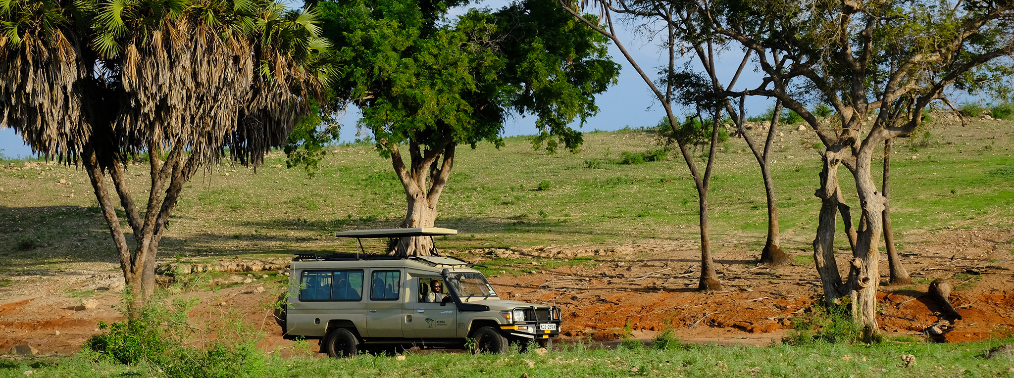 Safari vehicle on guided tour past river banks in Tsavo East National Park in Kenya.