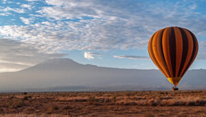 Panoramic views of a hot air balloon and Mount Kilimanjaro at sunrise.