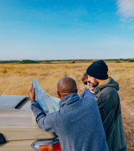 Two guests and a guide looking at a map lying on the top of a safari vehicle bonnet.