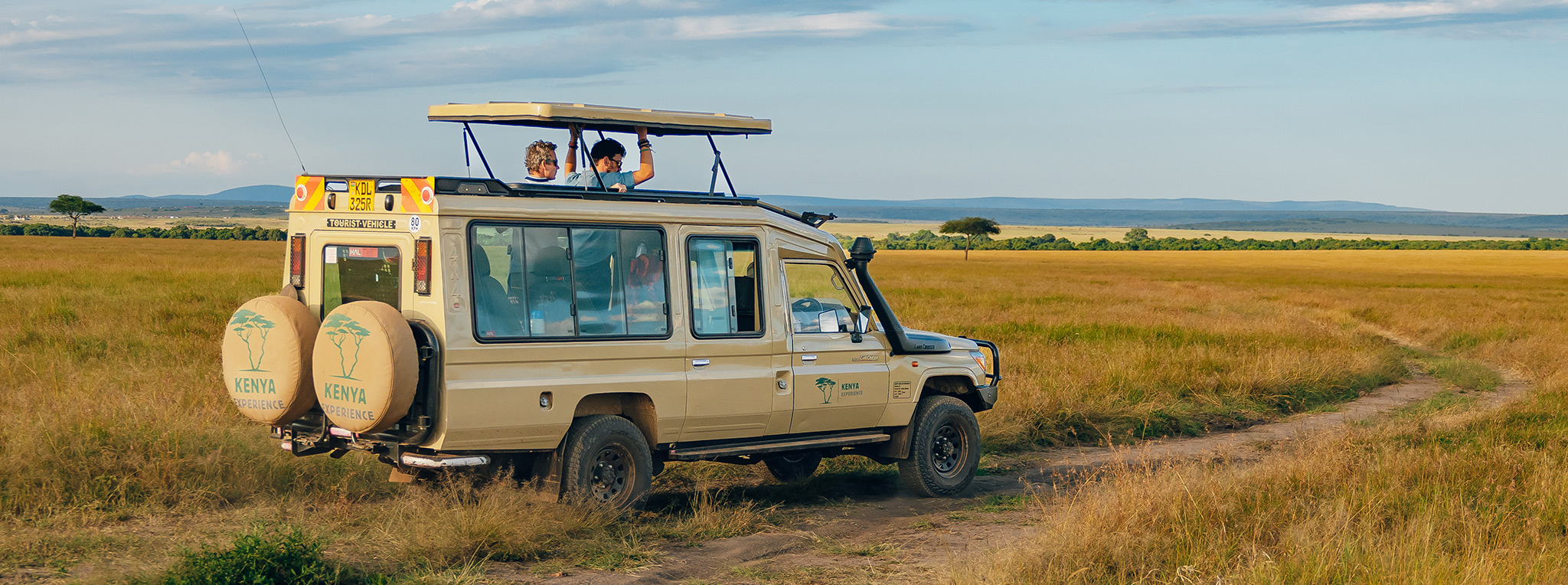 A safari vehicle with guests stands on the side of the road in the Masai Mara in Kenya.