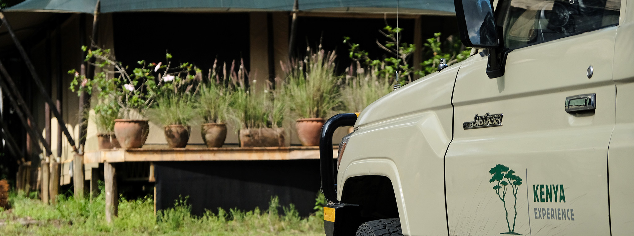 Am office tent with plants and a 4x4 vehicle parked in front of it, the setup of our Kenya safari tour operator business.