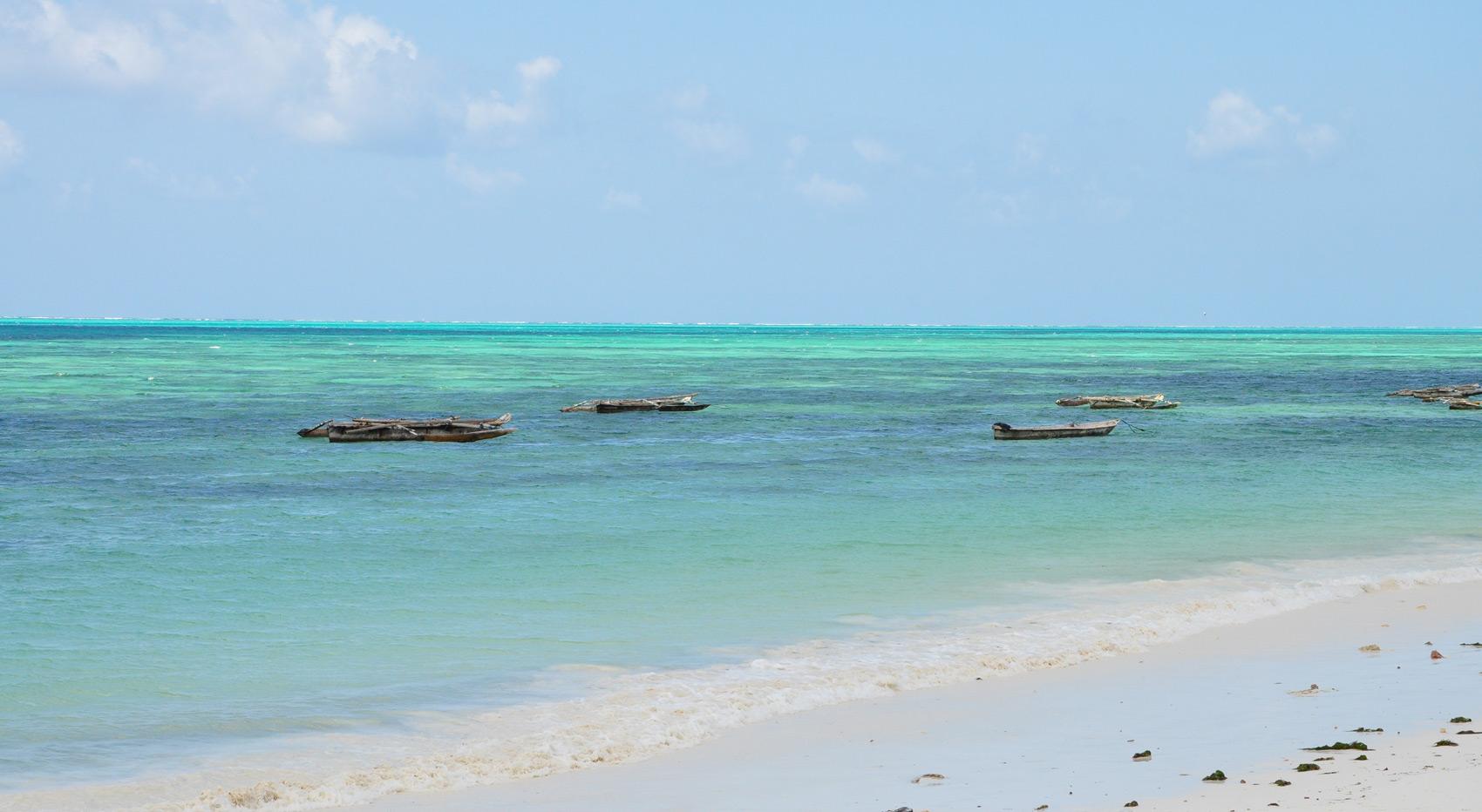 The Indian Ocean sways gently onto the shores of Zanzibar Island, boats anchored in the shallow. 