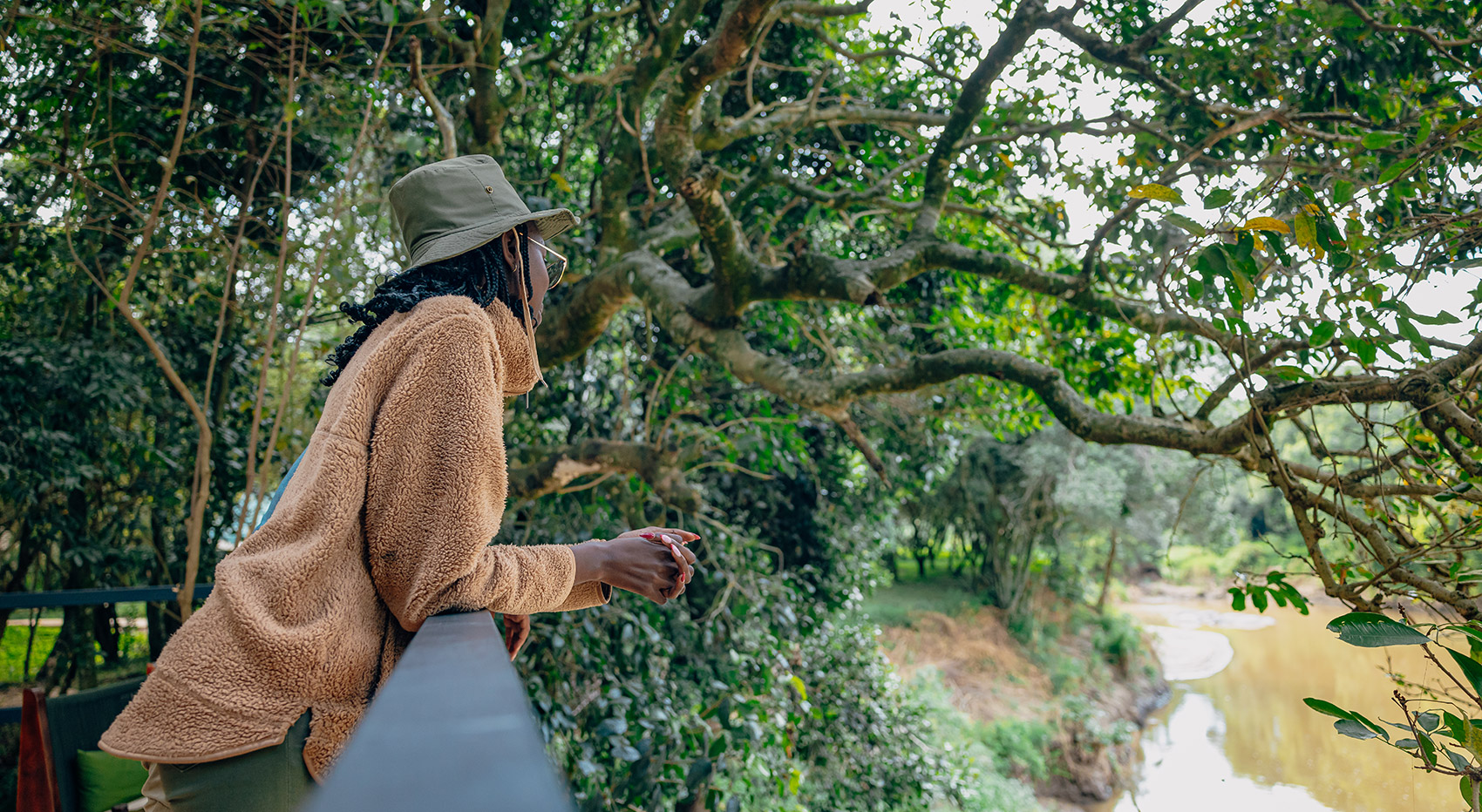 A woman traveller overlooking a river in a forested area from a viewing platform at Serenity Mara Legends Camp in the Maasai Mara.